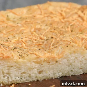 Parmesan and Herb Focaccia Recipe: Crispy, Fluffy Loaf 8 A close-up of a thick slice of Parmesan Herb Focaccia, topped with shredded cheese and herbs, showing a golden, slightly crisp crust and a soft, airy interior.