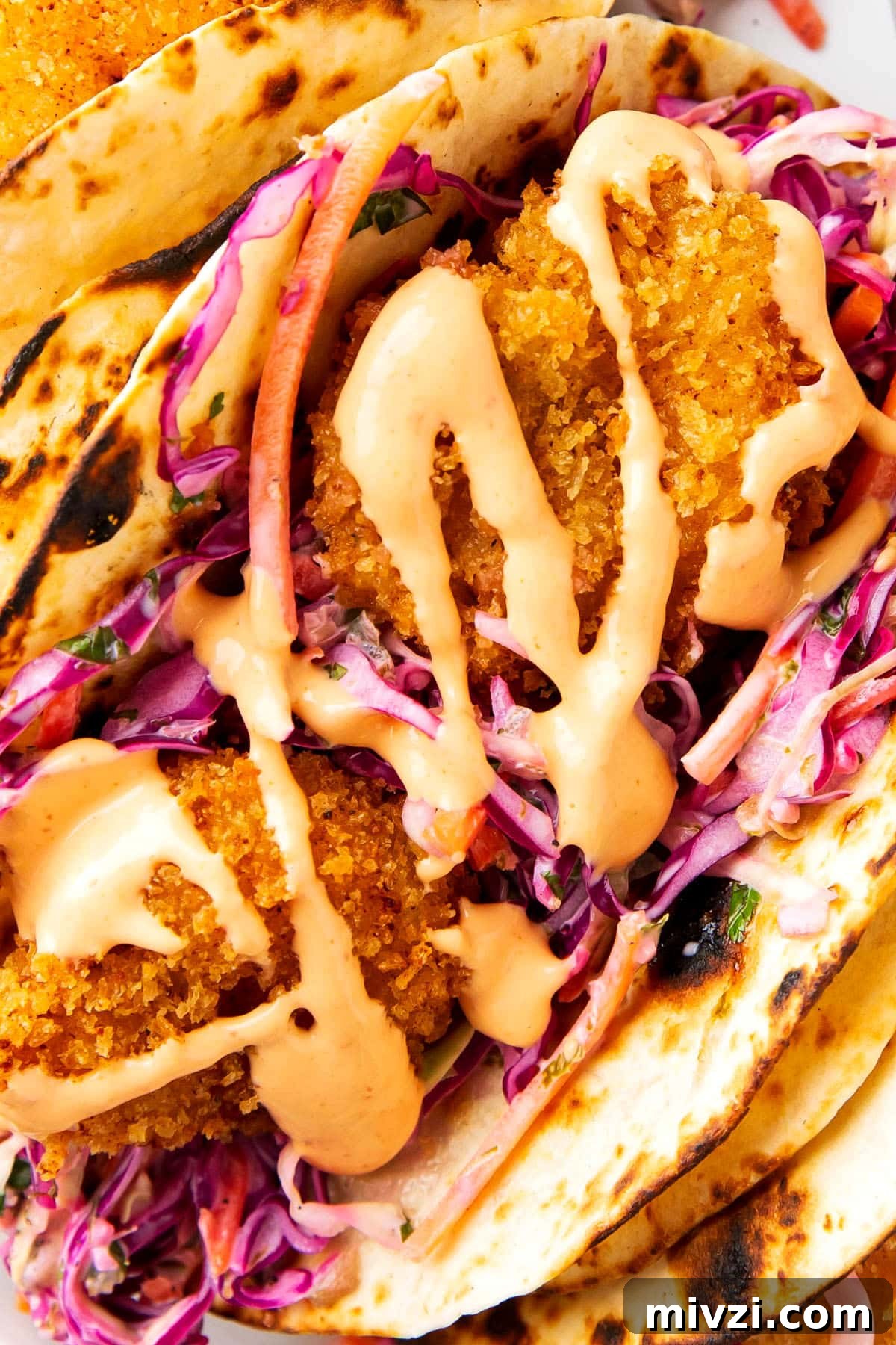 Crispy Panko Shrimp Tacos with Tangy Slaw 3 Close up of this fried shrimp tacos recipe shows the crunchy texture of crispy shrimp nestled in sliced red cabbage and tortillas served with sauce and fresh limes.