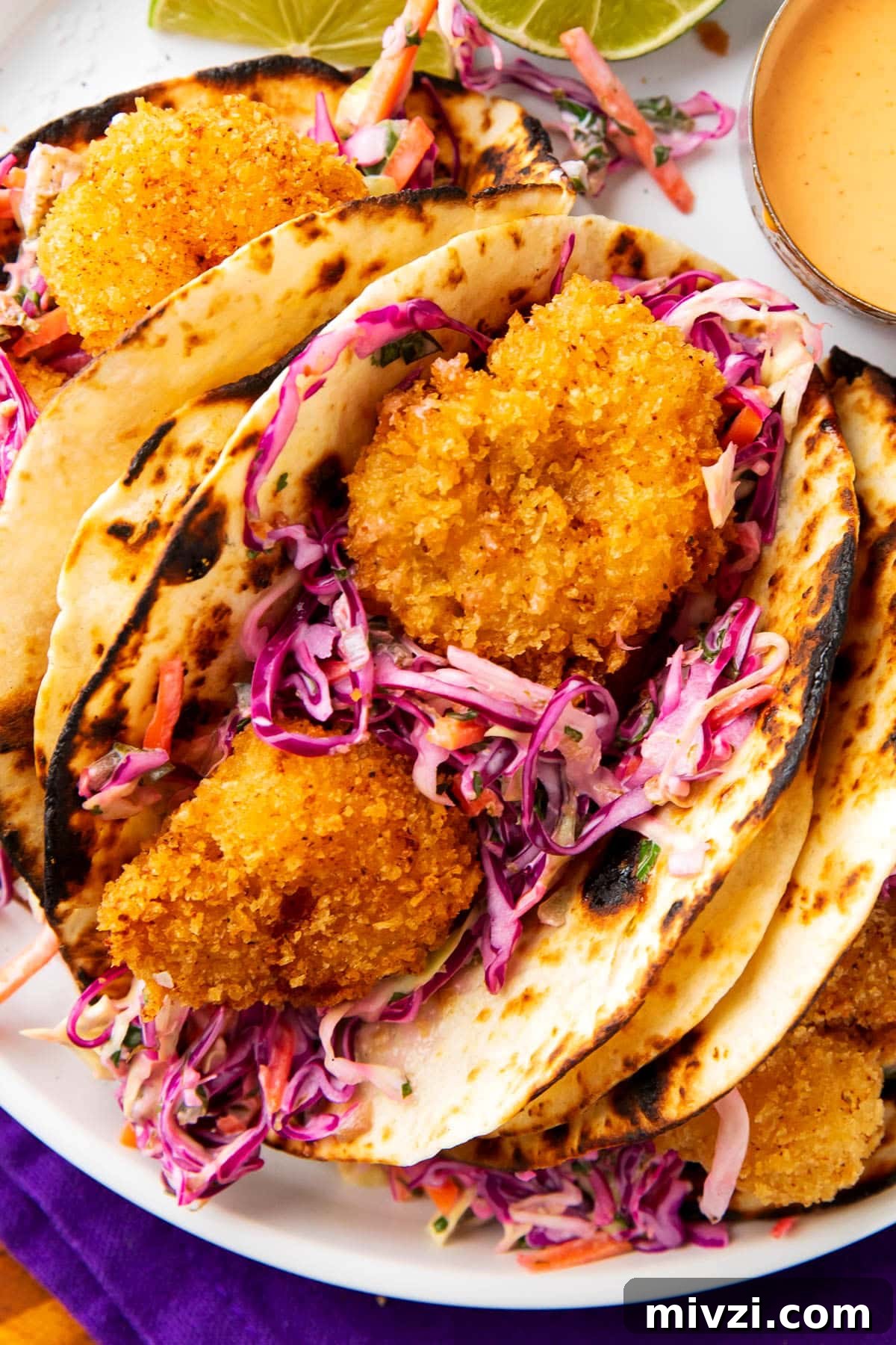 Crispy Panko Shrimp Tacos with Tangy Slaw 5 Crispy shrimp tacos recipe served on a plate with lots of golden fried shrimp, cilantro lime slaw, and a creamy sauce for drizzle.
