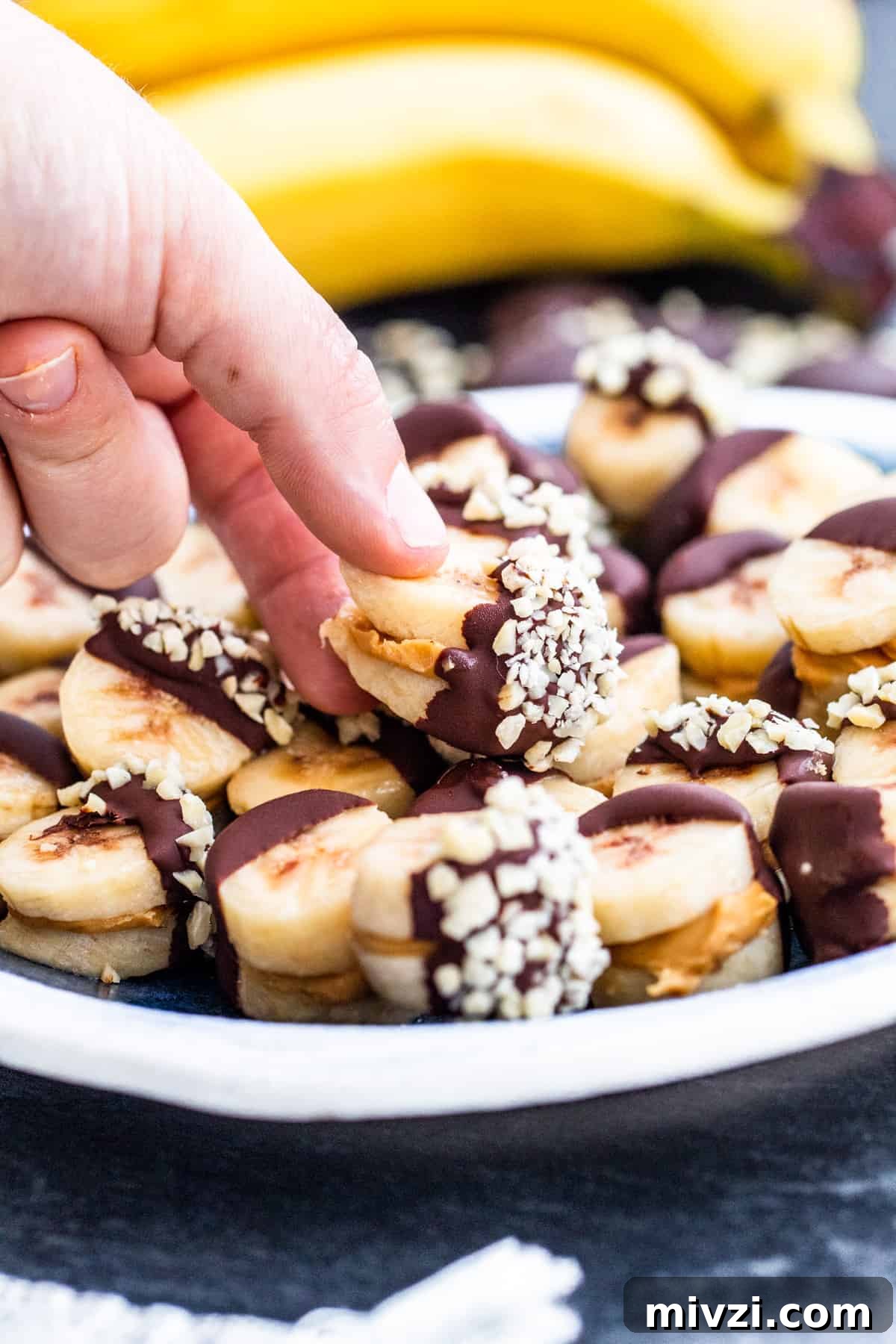 Hand picking up one banana peanut butter bite from plate.