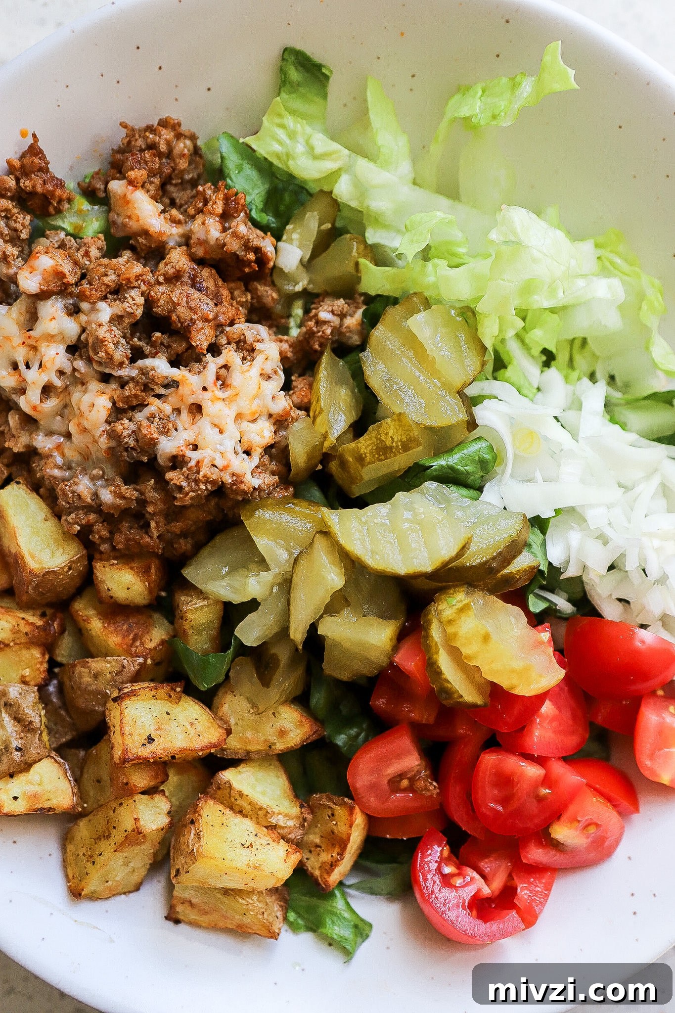 Top down view of ground beef, lettuce, tomatoes, potatoes and onions.