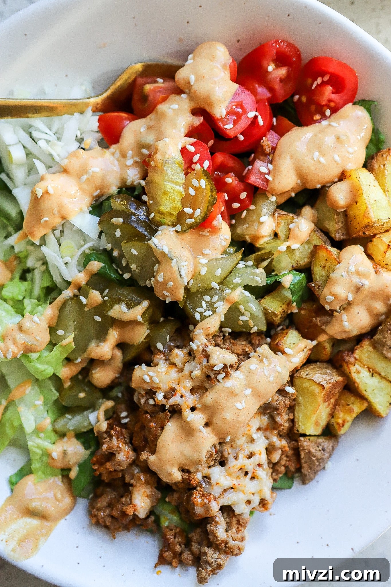 Top down view of a cheeseburger bowl with tomatoes, lettuce, ground beef, potatoes and special sauce.