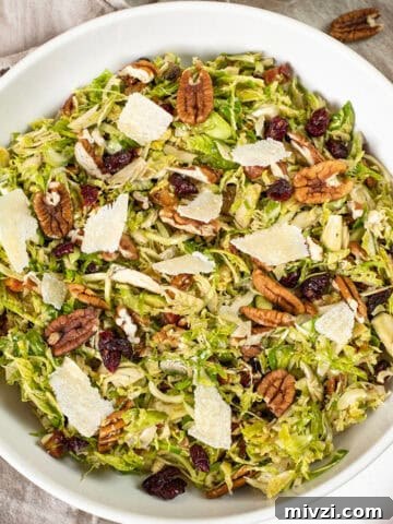 Brussels sprouts salad in a bowl topped with dried cranberries and pecans.