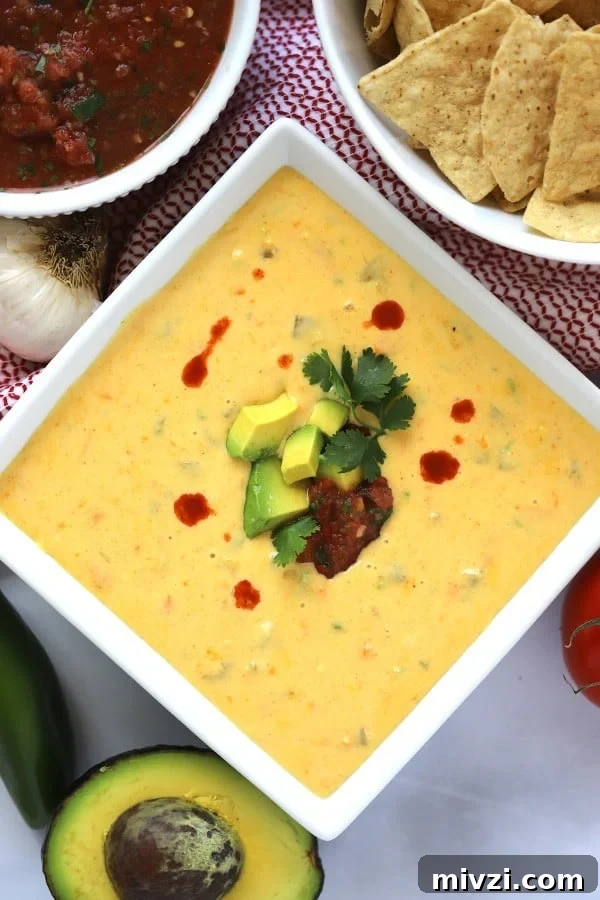 Cheddar Queso Dip recipe with chips on the side and hot sauce with avocado garnish; best cheddar cheese queso recipe.