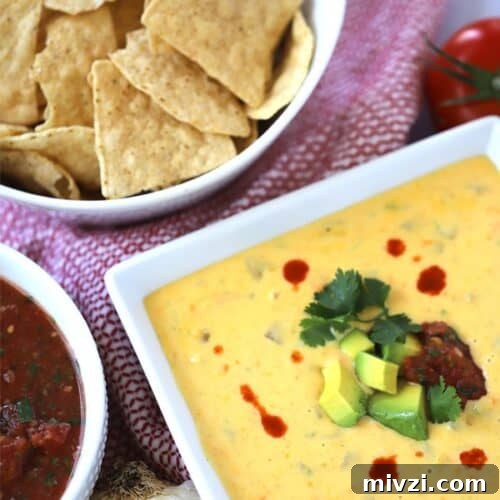 Cheddar queso dip in a bowl served with chips on the side
