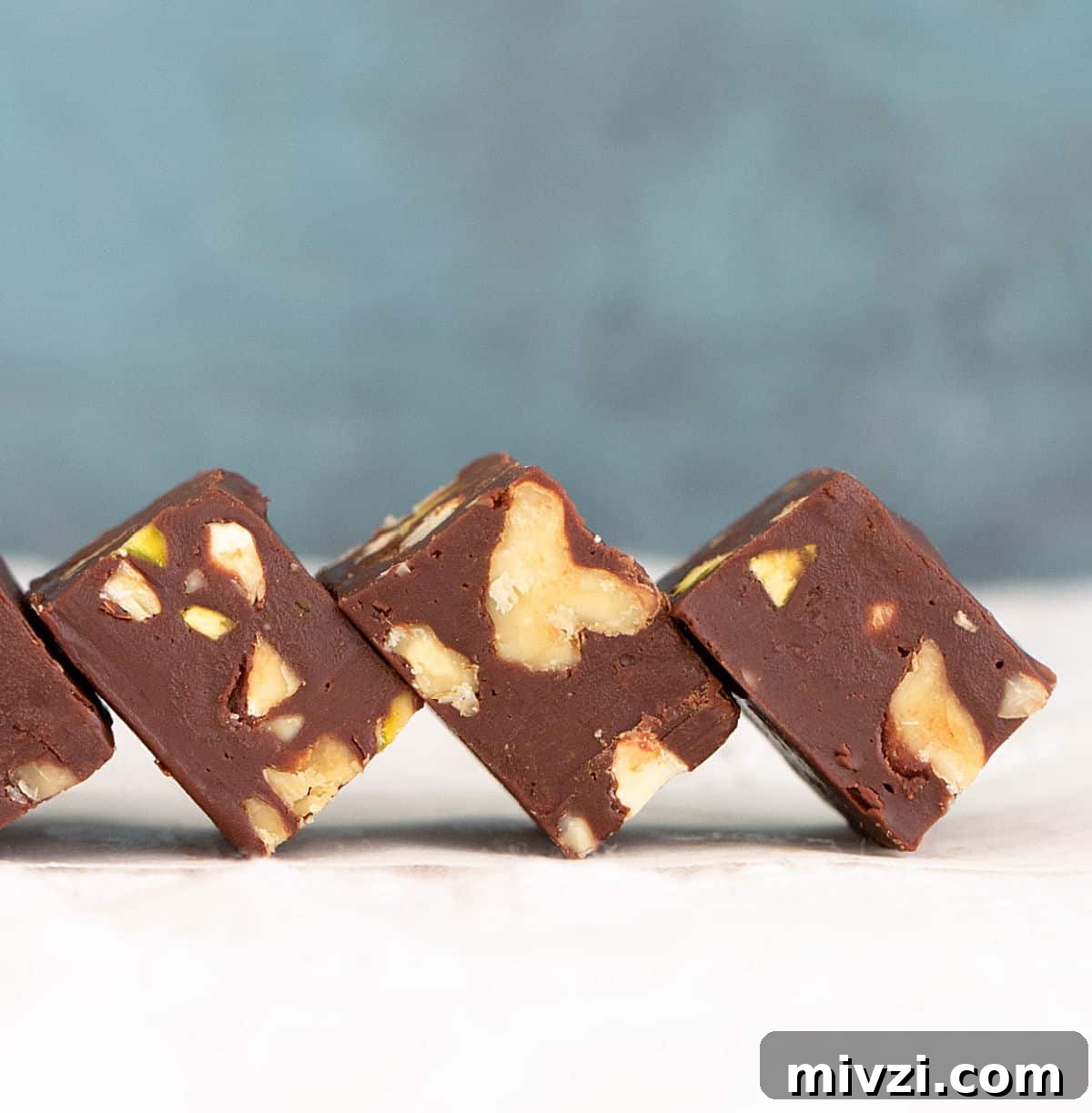 Quick Microwave Chocolate Fudge: Ready in Minutes 2 Row of leaning pieces of chocolate walnut squares with blue background and a white surface.
