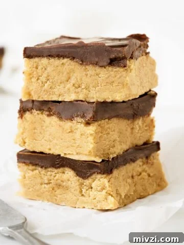 Three squares of peanut butter chocolate fudge on a white paper and white surface.