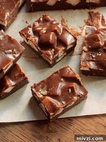 Top view of pieces of chocolate Marshmallow Fudge on white paper on a wooden table.