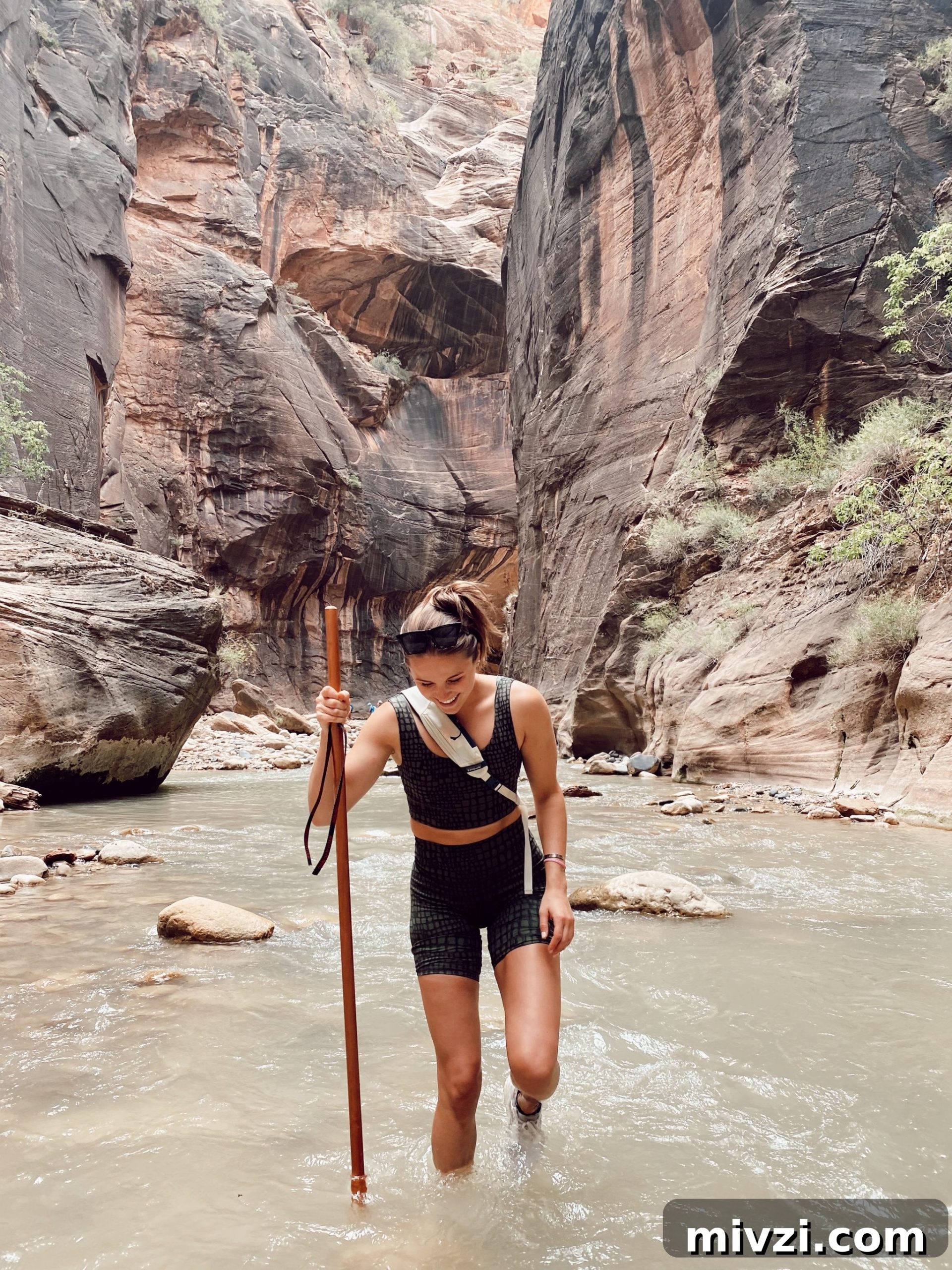 Girl smiling in water hiking with large stick in the middle of the Narrows