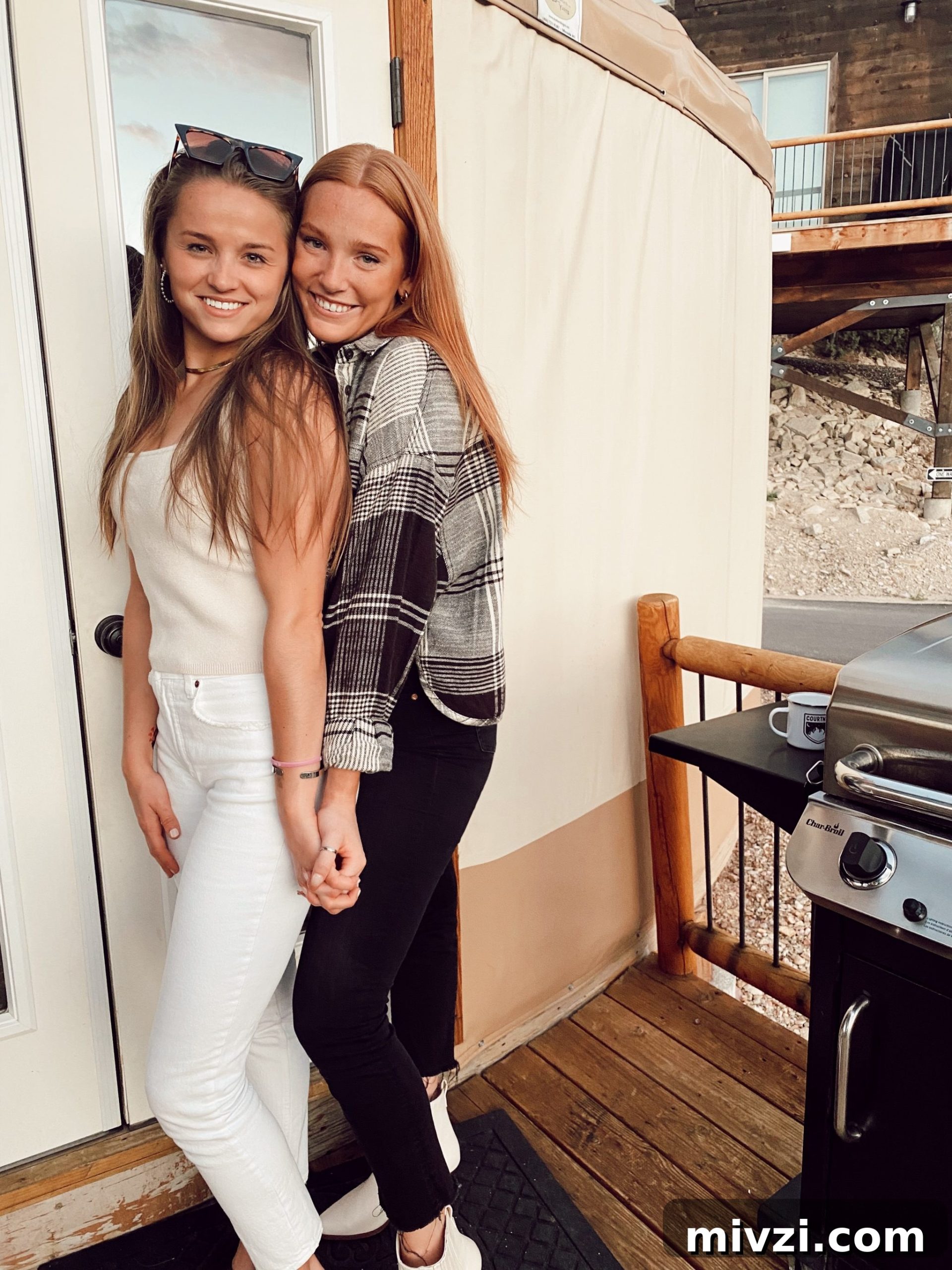 two girls standing together smiling and holding hands in front of the yurt
