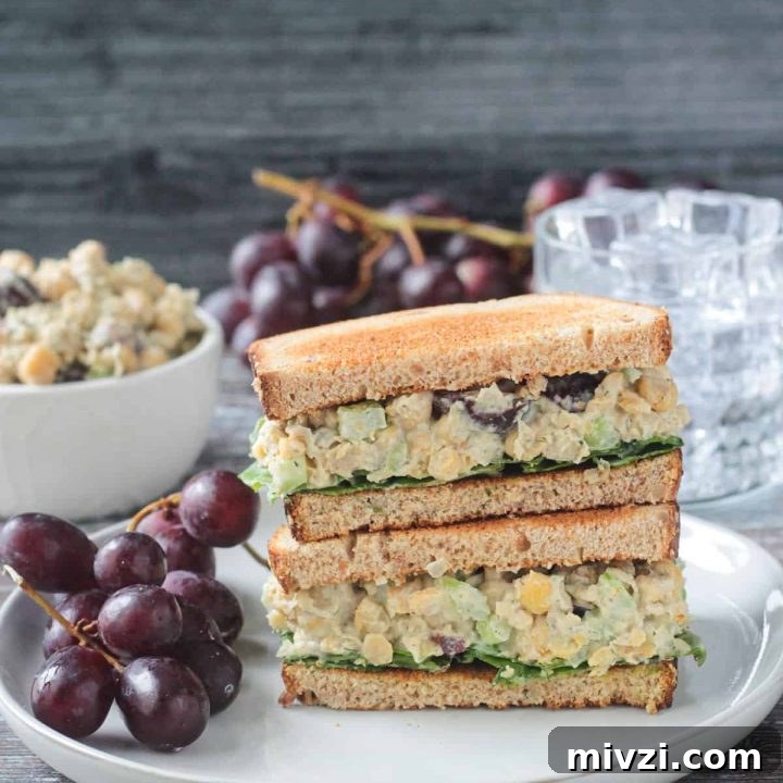 Stacked sandwich halves on a plate with a bunch of red grapes.