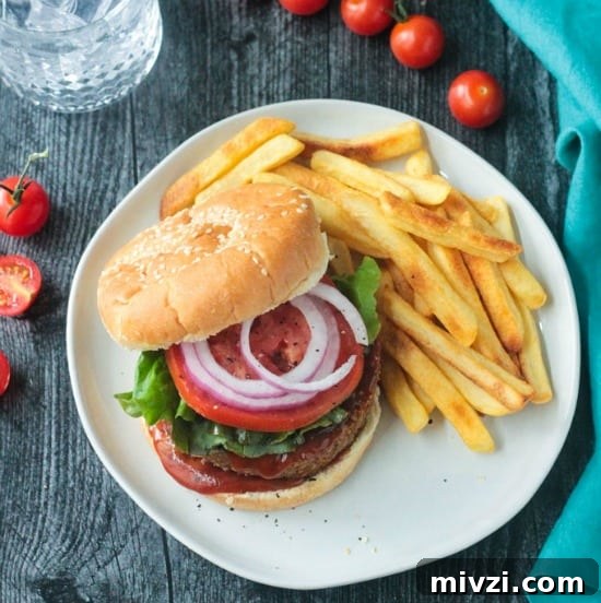 veggie burger on a bun with tomato, lettuce, red onion and bbq sauce next to a side of french fries