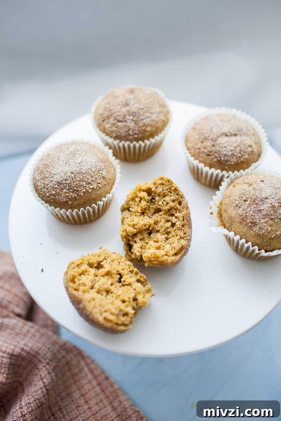 A pumpkin muffin split in half sitting on top of a white porcelain cake stand.