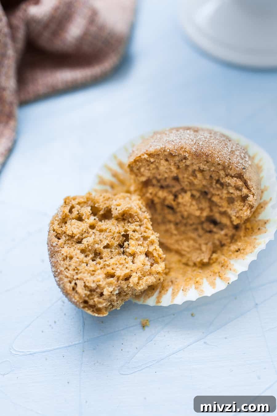 A pumpkin muffin, wrapped in a cupcake liner, cut in half on a light blue surface.