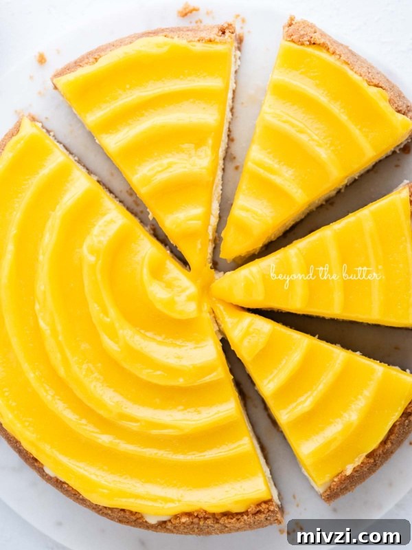 Lemon cheesecake topped with lemon curd cut into slices on a marble cake plate with white background.
