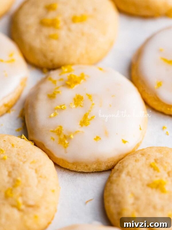 Lemon iced and plain lemon shortbread cookies garnished with lemon zest on white parchment paper.
