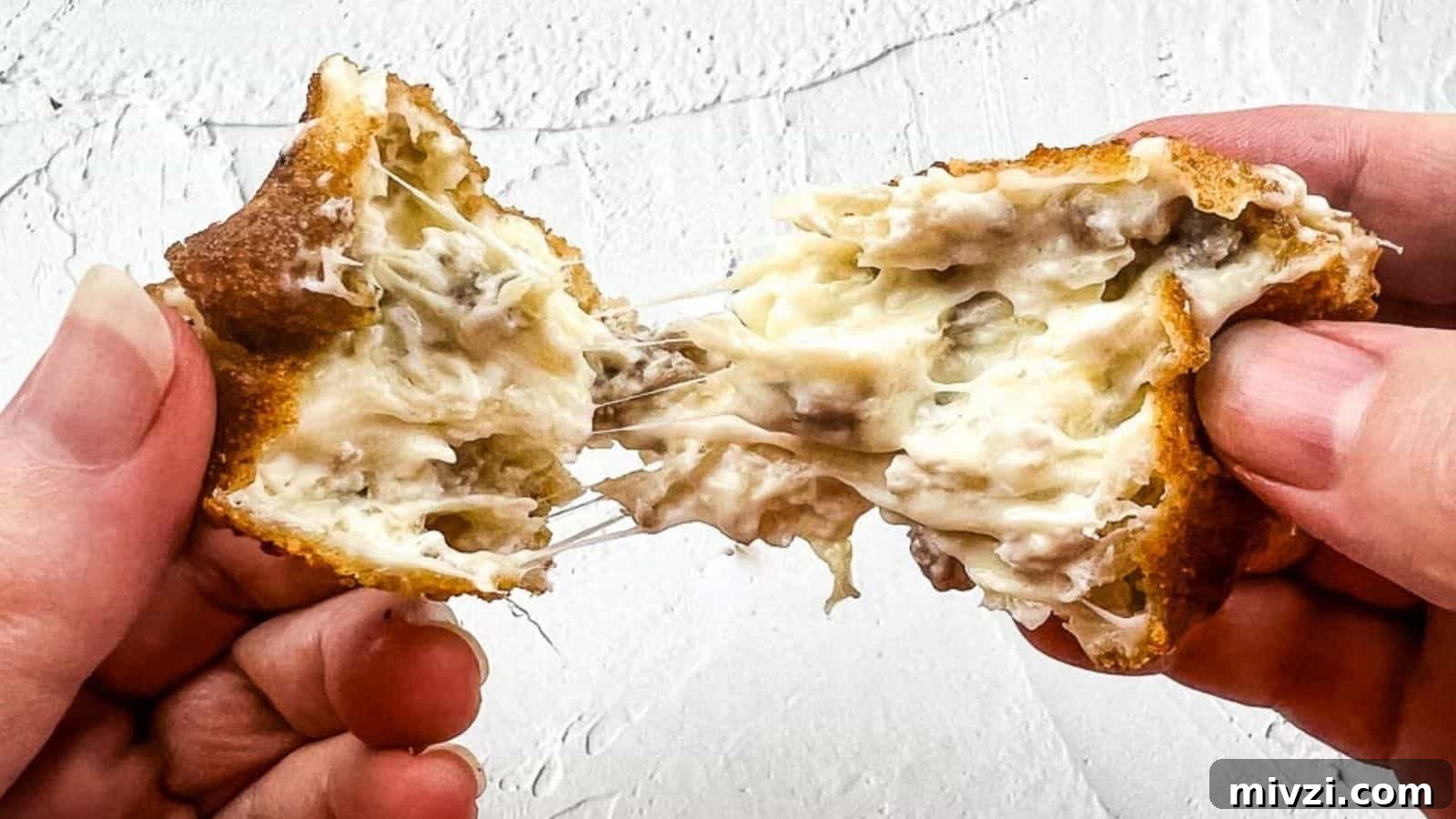 37 Winter Olympics Dishes to Warm Cold Nights and Long Broadcasts 11 A close-up shot of hands pulling apart a crispy, golden-brown, cheese-filled snack with a gooey, melted cheese center against a textured white background.