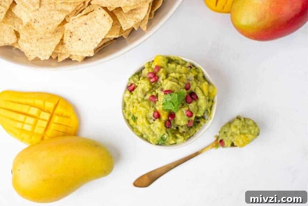 37 Winter Olympics Dishes to Warm Cold Nights and Long Broadcasts 13 A bowl of Tropical mango guacamole sits next to a spoon, tortilla chips, and two mangoes on a white surface.