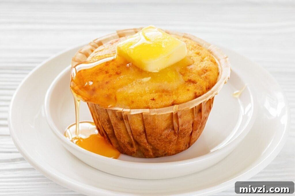 37 Winter Olympics Dishes to Warm Cold Nights and Long Broadcasts 18 A Honey Cornbread muffin on a white plate, topped with a pat of butter and drizzled with syrup.