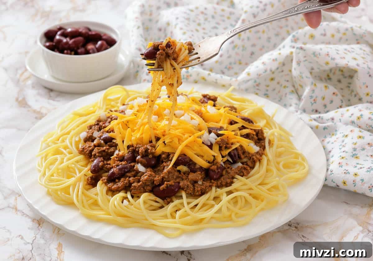 37 Winter Olympics Dishes to Warm Cold Nights and Long Broadcasts 19 A plate of spaghetti topped with Cincinnati chili, kidney beans, and shredded cheddar cheese, with a fork lifting a portion.