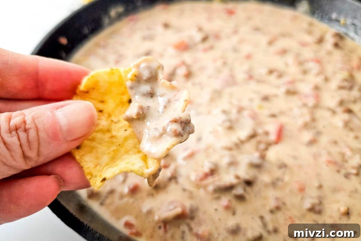 37 Winter Olympics Dishes to Warm Cold Nights and Long Broadcasts 30 A hand holding a tortilla chip with creamy Queso Blanco Rotel Dip, over a skillet filled with the same dip.