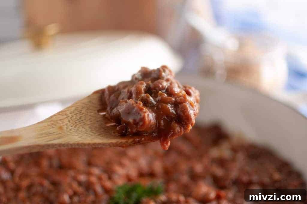 37 Winter Olympics Dishes to Warm Cold Nights and Long Broadcasts 31 A wooden spoon holds a serving of Baked Bean Casserole above a pot filled with more bean casserole.