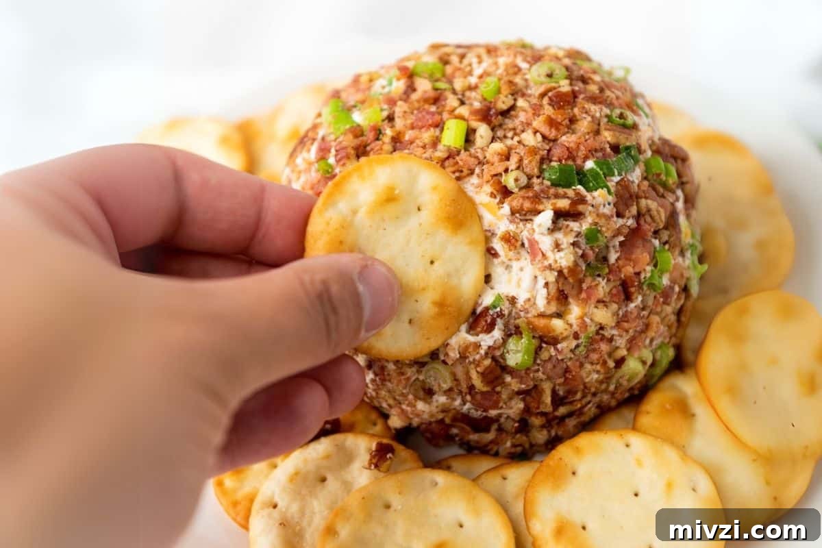 37 Winter Olympics Dishes to Warm Cold Nights and Long Broadcasts 37 A hand holding a round cracker, reaching to dip into a pecan bacon cheeseball.