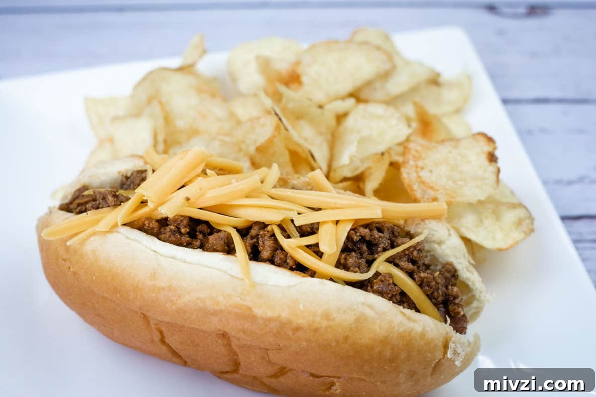 37 Winter Olympics Dishes to Warm Cold Nights and Long Broadcasts 5 A hot dog chili topped with shredded cheddar, served with potato chips on a white plate.