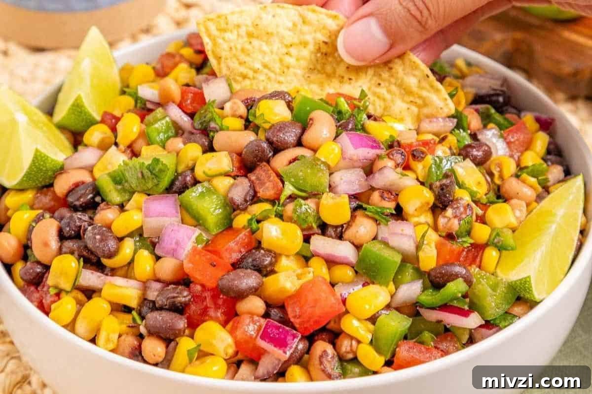 37 Winter Olympics Dishes to Warm Cold Nights and Long Broadcasts 7 A bowl of Cowboy Caviar, garnished with lime wedges; a hand dips a tortilla chip into the salad.