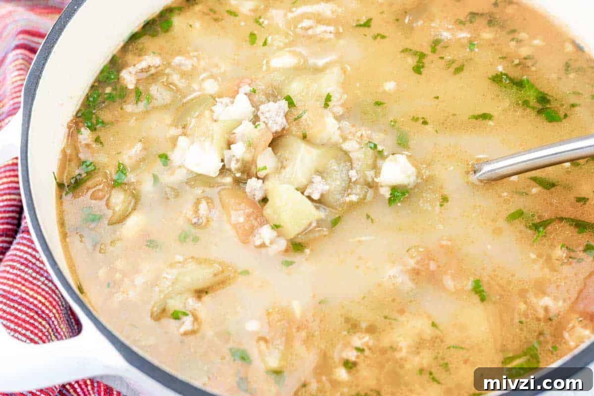 37 Winter Olympics Dishes to Warm Cold Nights and Long Broadcasts 9 A pot of Green pork posole soup with ground meat, vegetables, herbs, and broth, with a metal ladle resting inside.