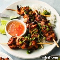 Grilled chicken skewers with green herbs, rice, lime wedges, and dipping sauce.