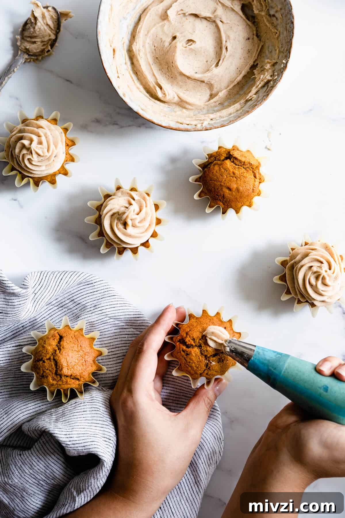 a person piping chai frosting on top of pumpkin cupcakes