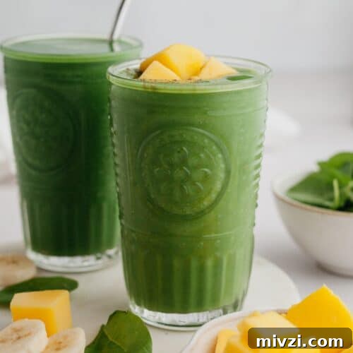 Two green smoothies in glasses, one has mango pieces on top.