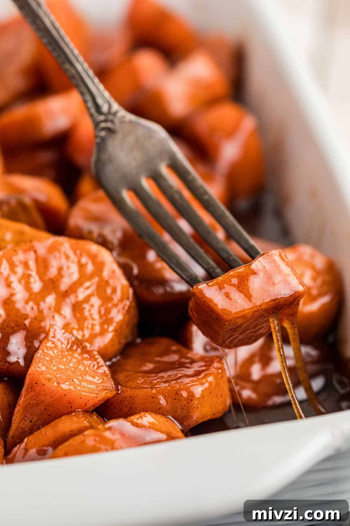 Southern-Style Candied Yams with Brown Sugar Glaze 12 A fork digging into a dish full of candied yams, a gooey sticky treacle oozing down.