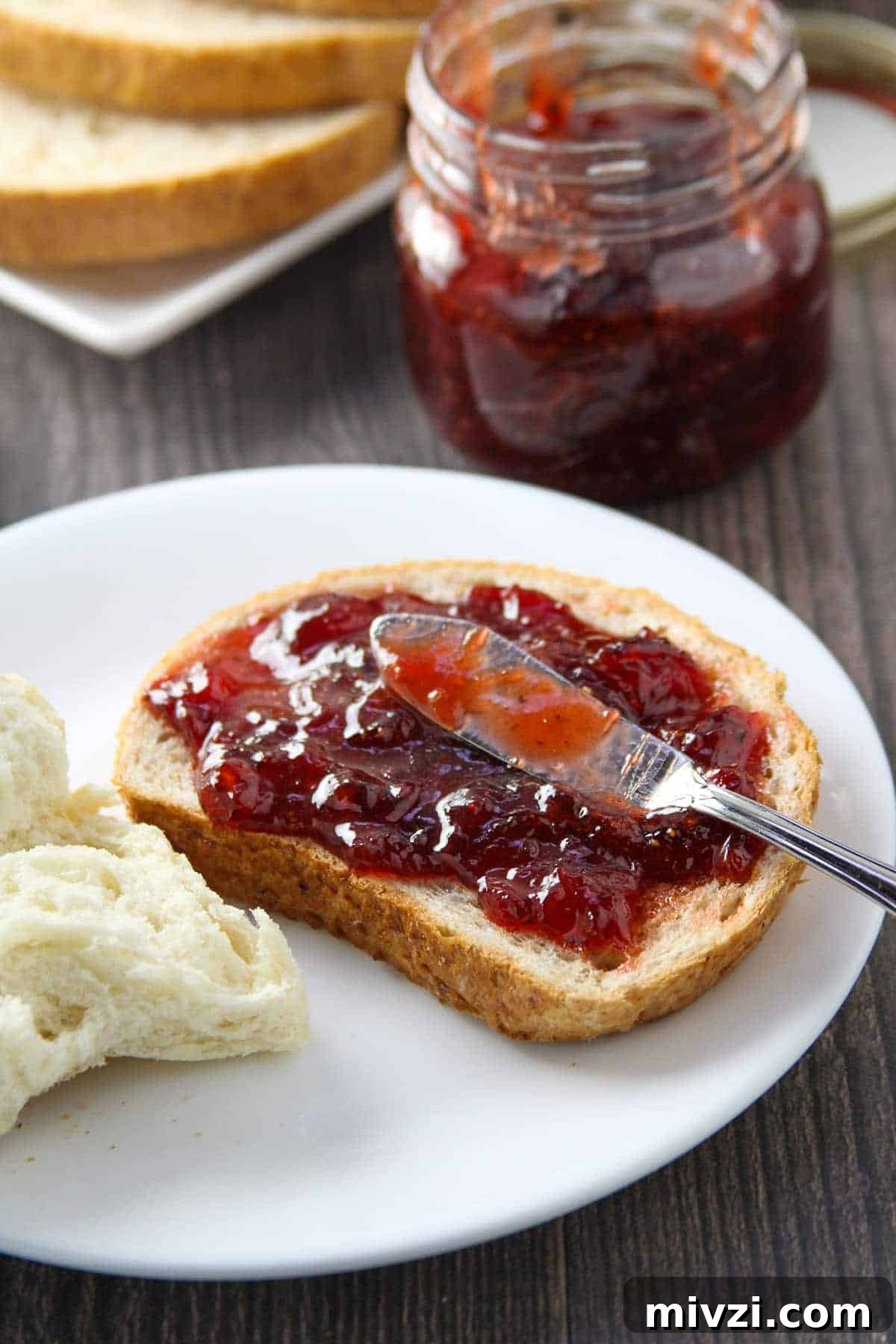 Strawberry Jam with Cracked Black Pepper: Sweet & Spicy Preserve 5 wheat toast with black pepper strawberry jam on a white plate with jar of jam on the side.