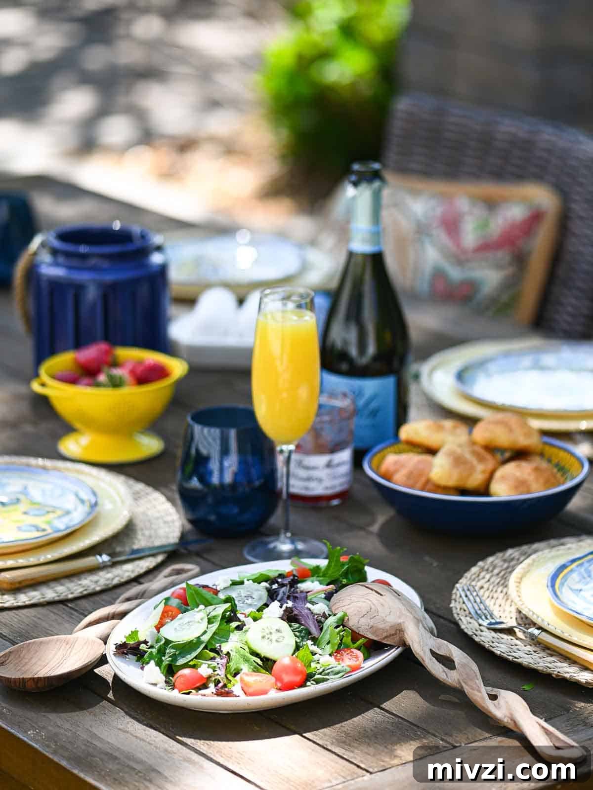 Casual outdoor brunch served on a wooden table with food and beverages in the background.
