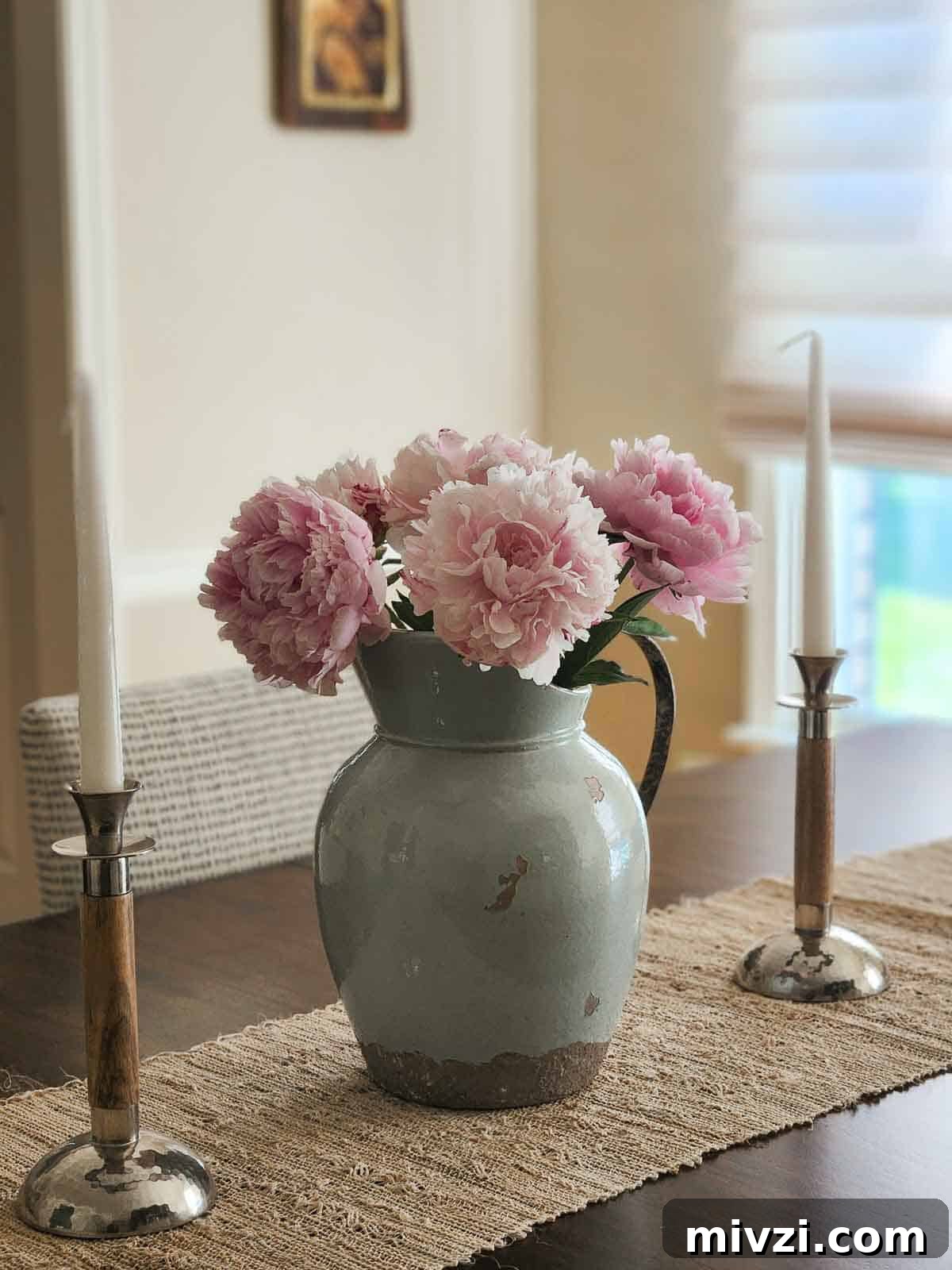 A blue antique pitcher with pink peonies on a wooden table.