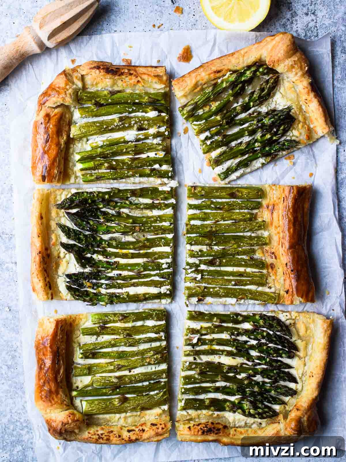 Overhead of asparagus and whipped goat cheese puff pastry tart cut into six pieces with a lemon to the side
