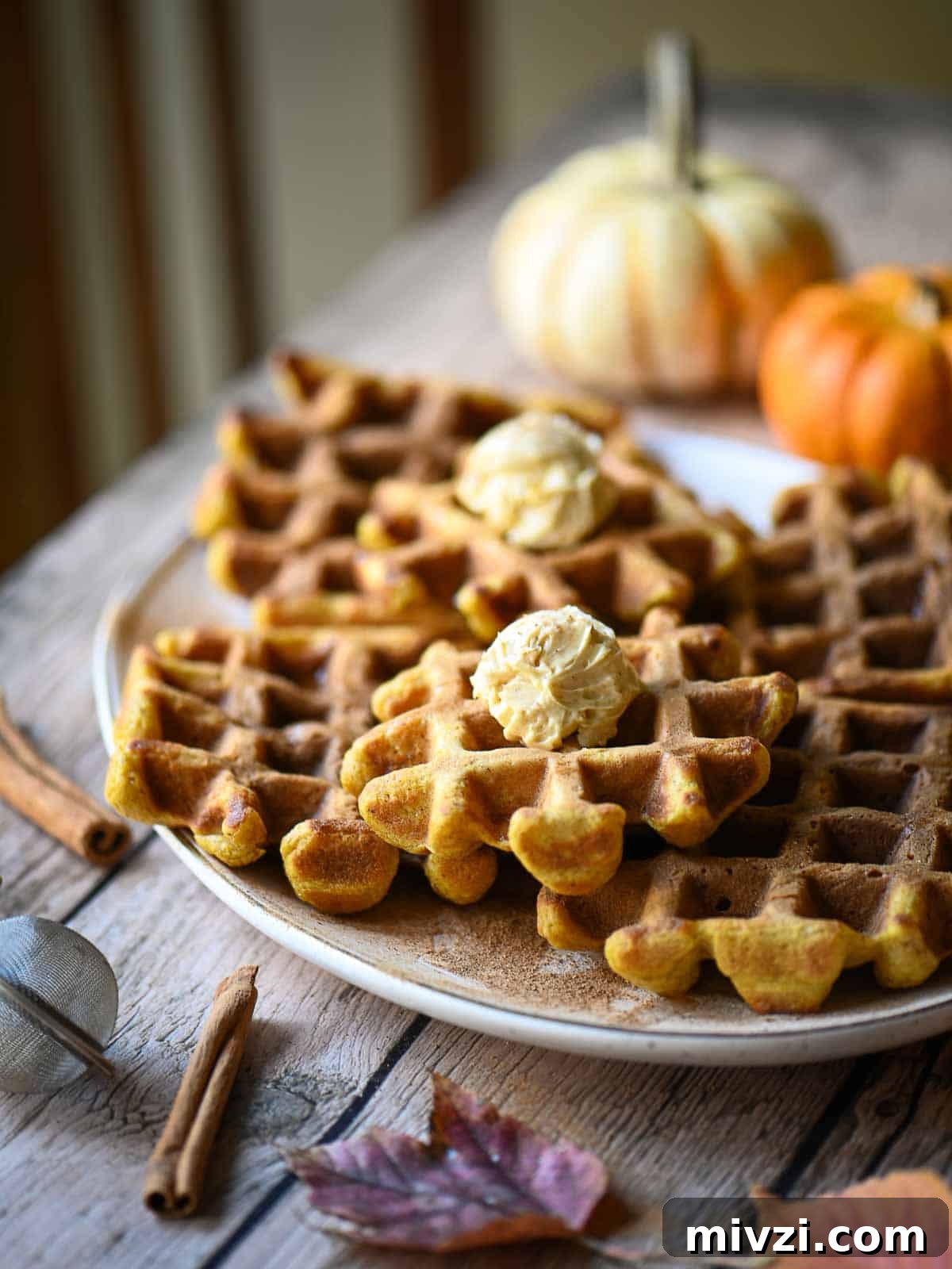 A platter of waffles on a wooden table with pumpkins in the background.
