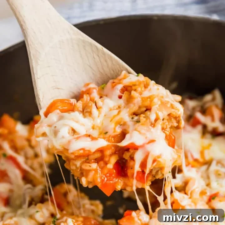 A wooden spoon pulling a a scoop of unstuffed peppers from the skillet.