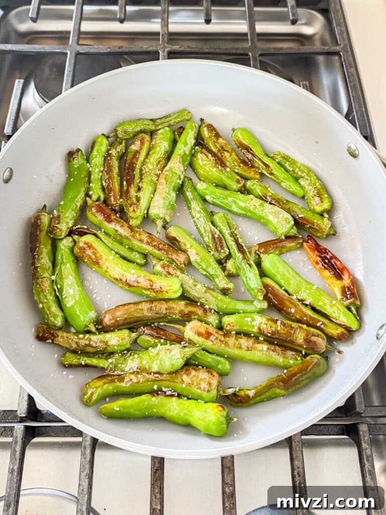 Blistered shishito peppers in a pan on the stove.