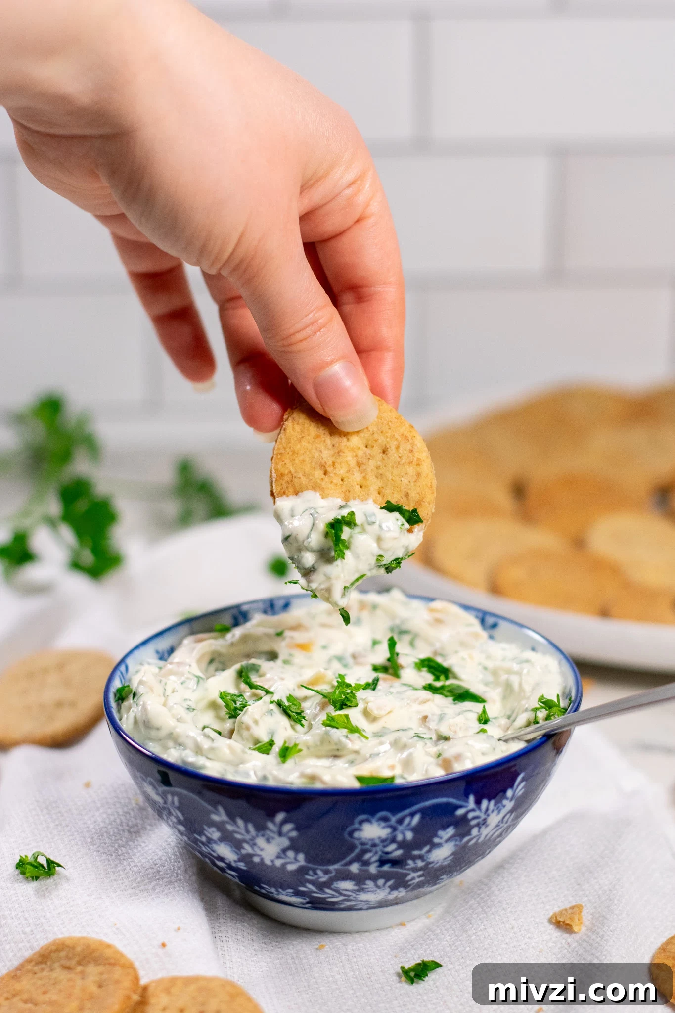 A person dipping a cracker into dip in a bowl.