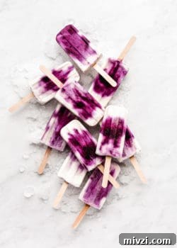 blueberry greek yogurt popsicles stacked on ice on a marble board