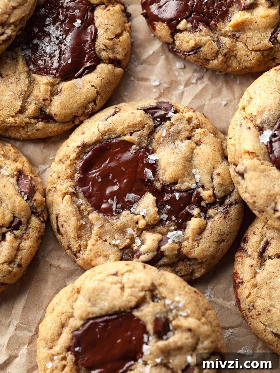 gluten free sourdough discard chocolate chip cookies on parchment paper topped with flaky sea salt. made with brown butter