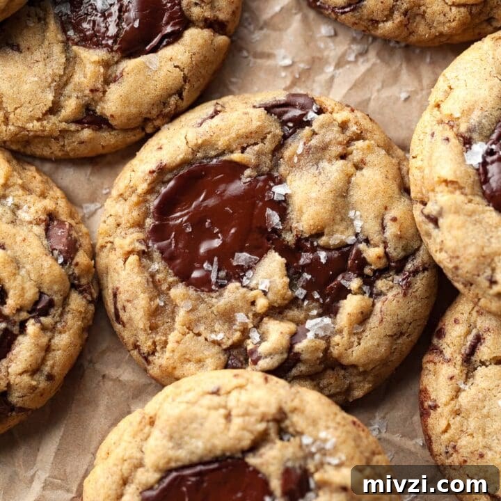 gluten free sourdough discard chocolate chip cookies on parchment paper topped with flaky sea salt. made with brown butter