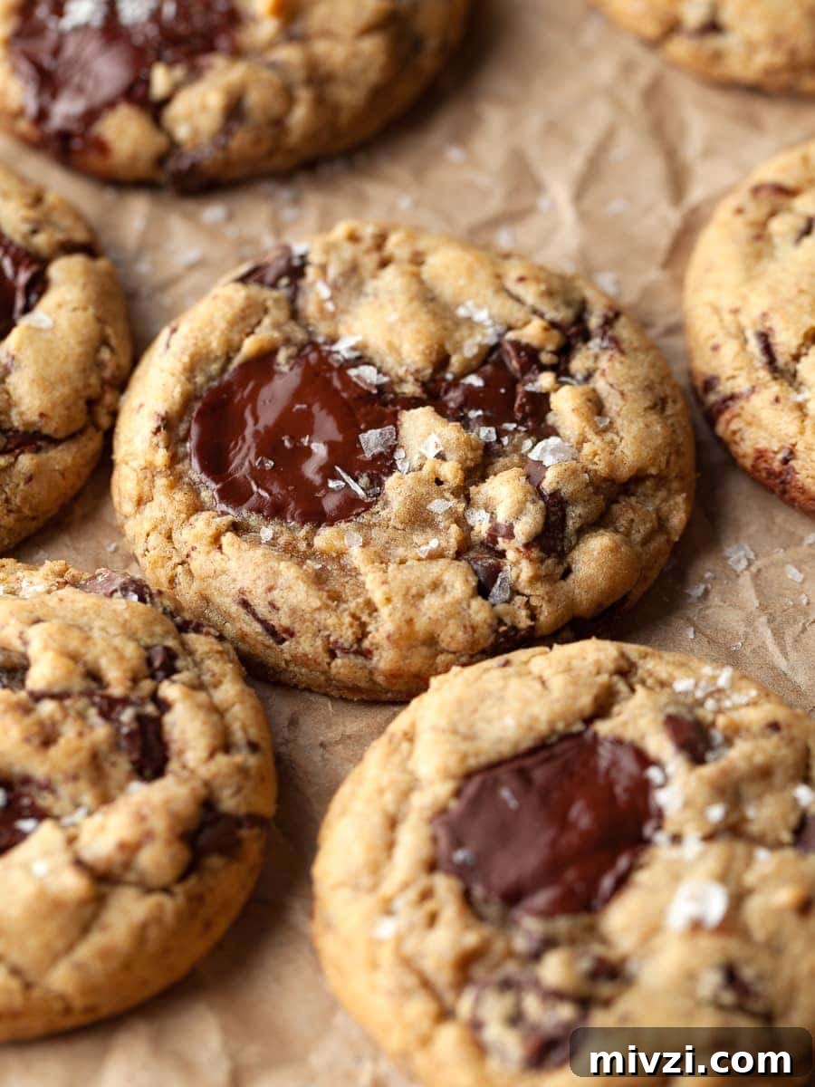 gluten free sourdough discard chocolate chip cookies on parchment paper topped with flaky sea salt. made with brown butter