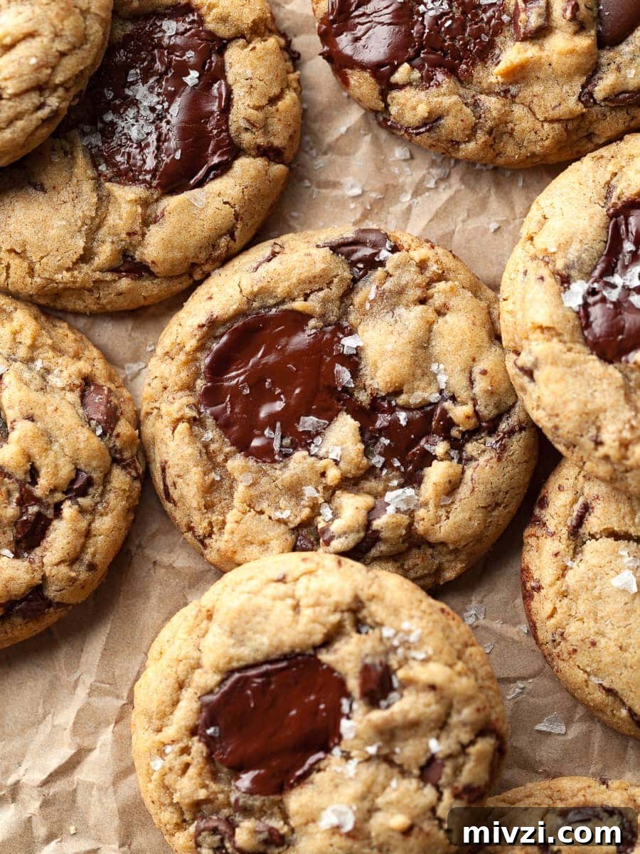 gluten free sourdough discard chocolate chip cookies on parchment paper topped with flaky sea salt. made with brown butter