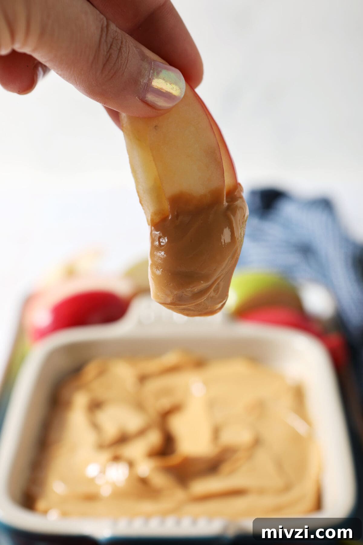 Creamy Dulce de Leche Dip Recipe for Desserts and Snacks 6 A hand holds an apple slice dipped in Dulce de Leche Caramel Dip above a platter
