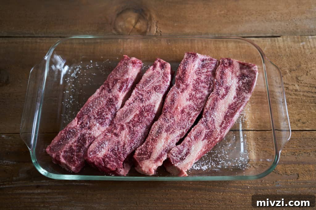 Beef short ribs in a glass casserole dish with salt on top.