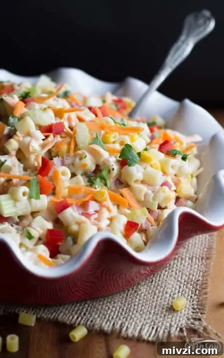 Rainbow pasta salad in a red and white ceramic dish on a wooden surface